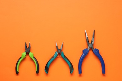 Different pliers on orange background, flat lay. Space for text