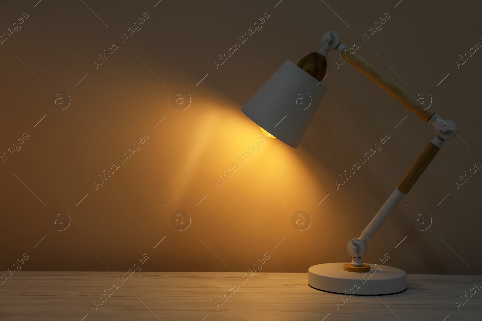 Photo of Stylish modern desk lamp on wooden table at night, space for text