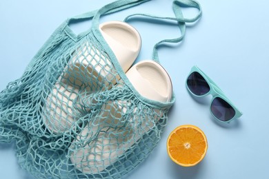 Photo of String bag, sunglasses, orange and slippers on light blue background, top view