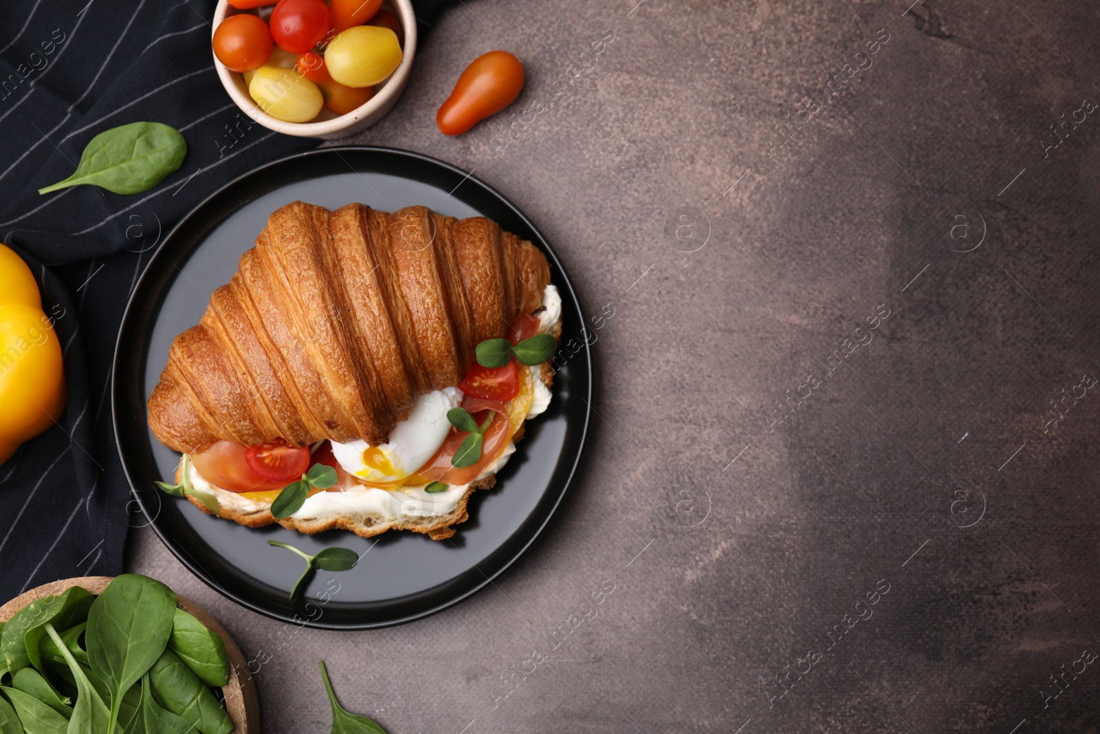 Photo of Tasty croissant with fried egg, tomato and microgreens on brown textured table, flat lay. Space for text