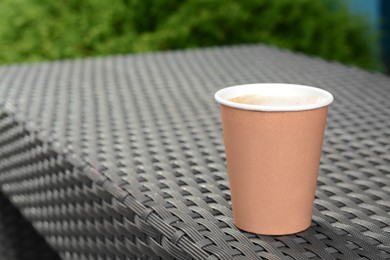 Photo of Coffee cardboard cup on rattan table outdoors, closeup. Space for text
