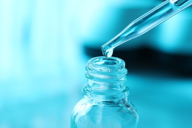 Dripping liquid from pipette into glass bottle on light blue background, closeup