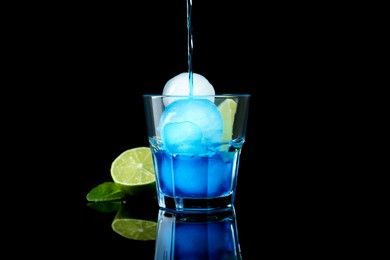 Photo of Pouring tasty cocktail into glass with ice balls on black background