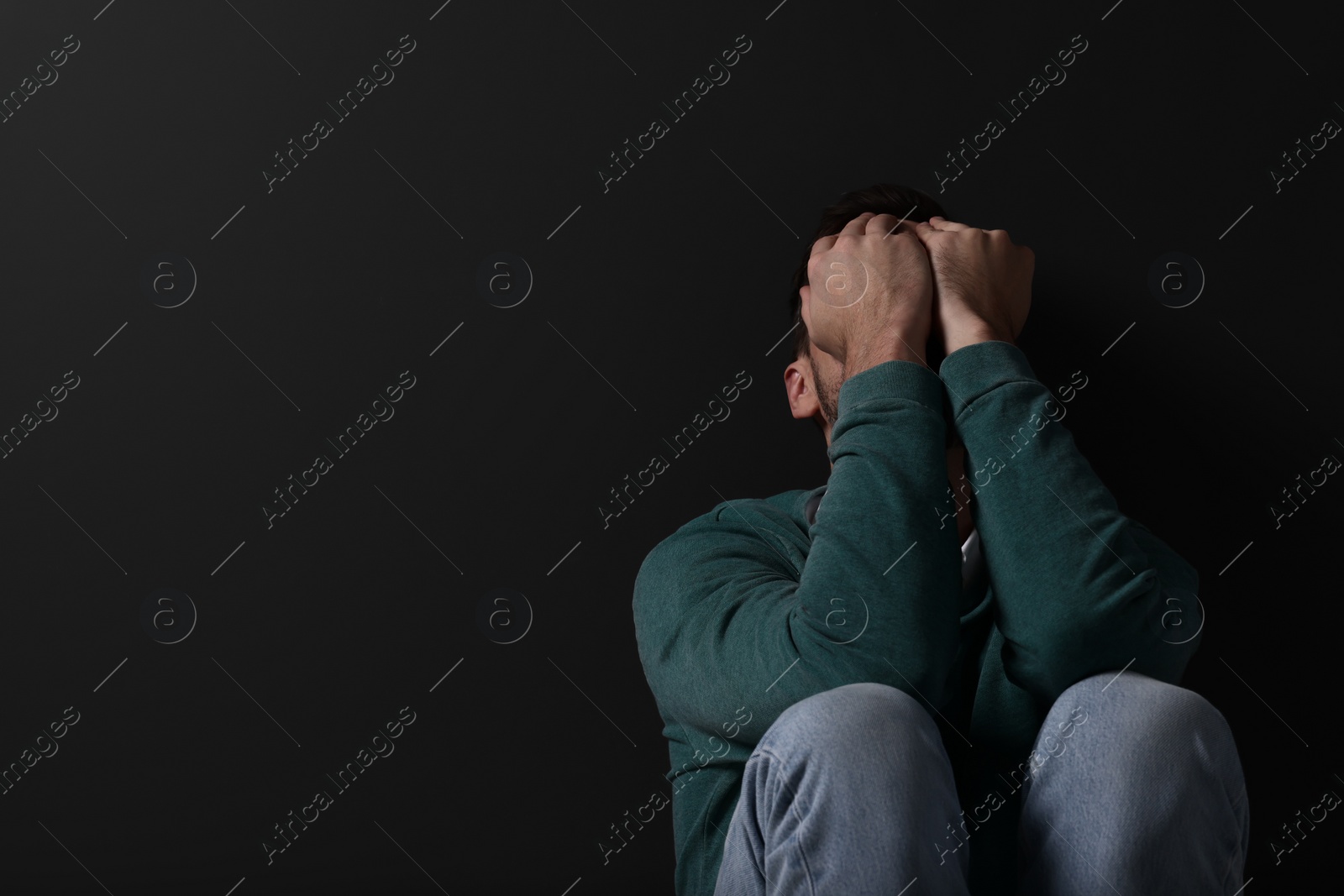 Photo of Upset man sitting on black background. Space for text
