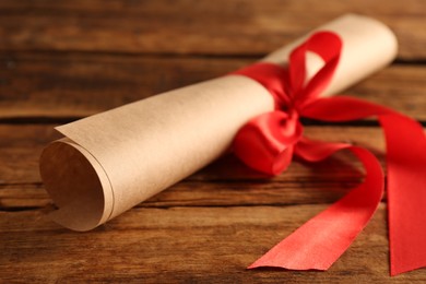 Photo of Rolled student's diploma with red ribbon on wooden table, closeup
