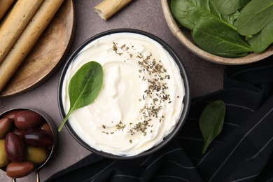 Delicious cream cheese, grissini sticks, olives and basil leaves on grey table, flat lay