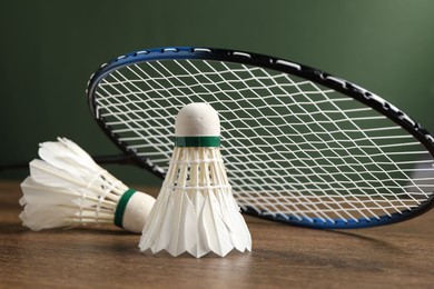 Feather badminton shuttlecocks and racket on wooden table against green background, closeup. Space for text