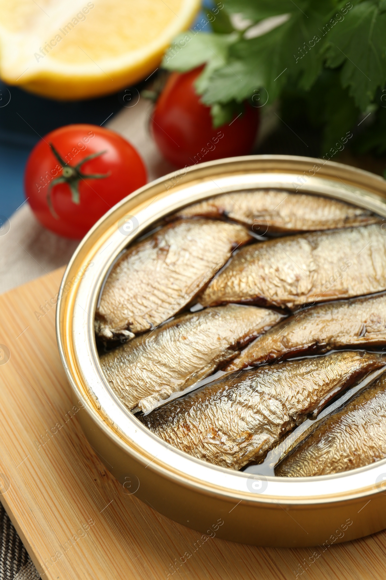 Photo of Tin can with tasty sprats served on wooden board, closeup