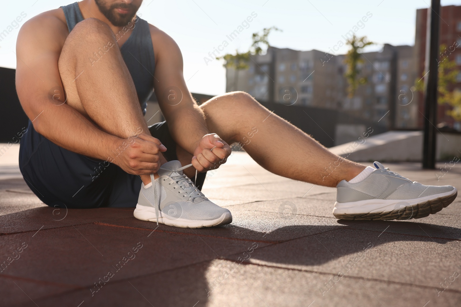 Photo of Man tying shoelaces before running outdoors on sunny day, closeup