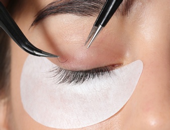 Young woman undergoing eyelashes extensions procedure, closeup