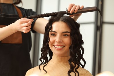 Hair styling. Hairdresser curling woman's hair in salon, closeup