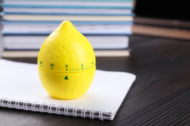 Photo of Kitchen timer in shape of lemon and notebook on wooden table, closeup. Space for text