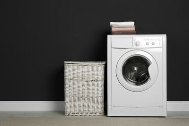 Modern washing machine and laundry basket near black wall