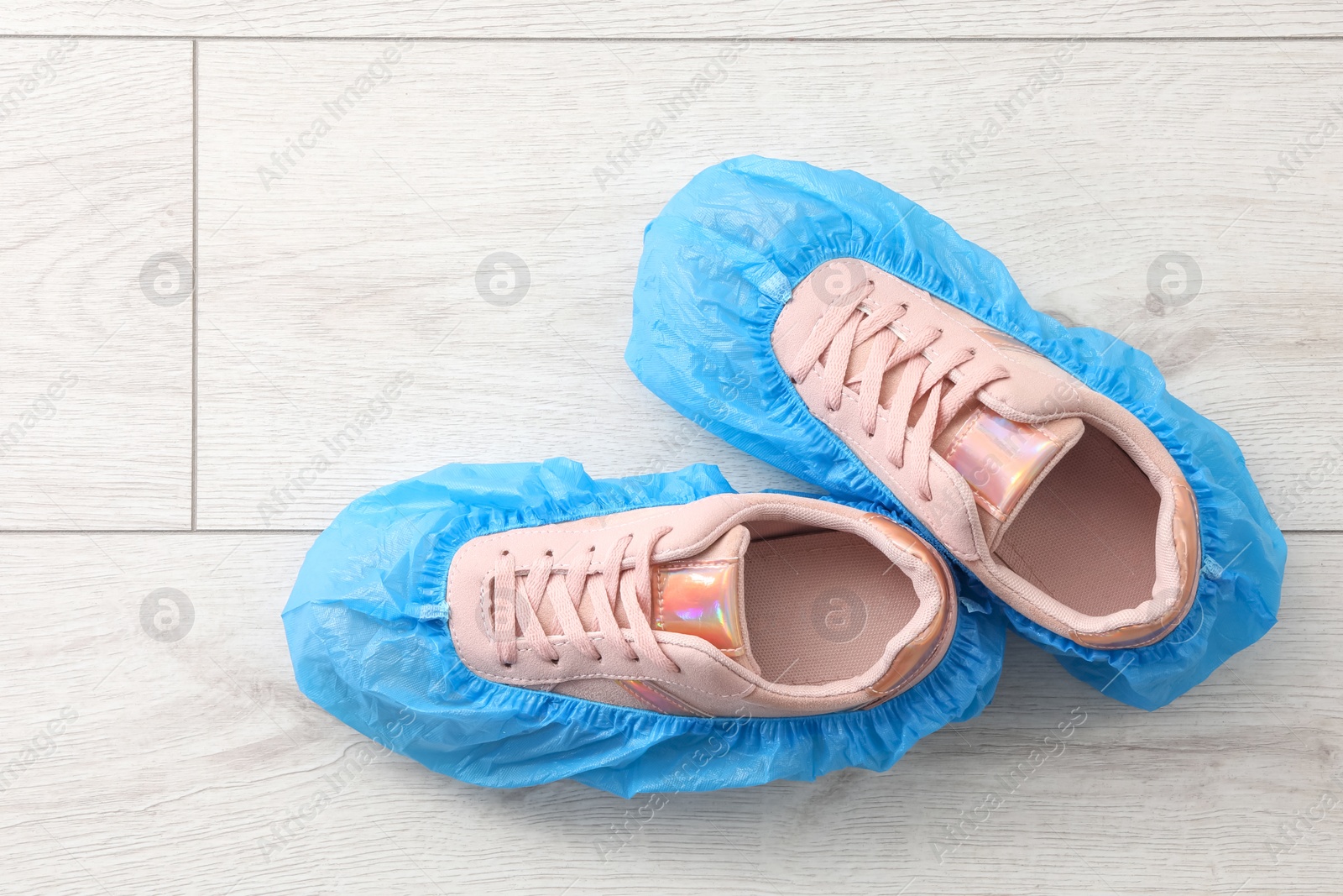 Photo of Women`s sneakers in blue shoe covers on light wooden floor, top view