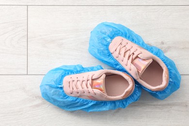 Women`s sneakers in blue shoe covers on light wooden floor, top view