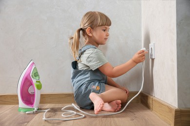 Photo of Little child playing with electrical socket and iron plug at home. Dangerous situation