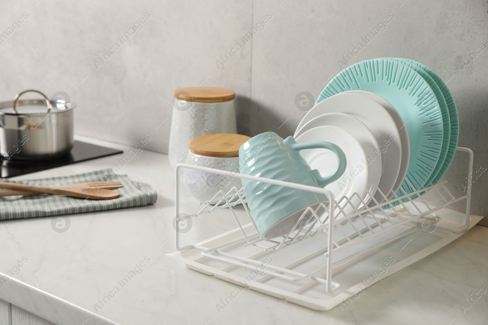 Photo of Drainer with different clean dishware and cup on light table indoors