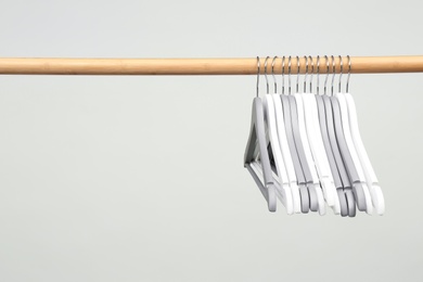 Photo of Empty clothes hangers on wooden rail against light background. Space for text