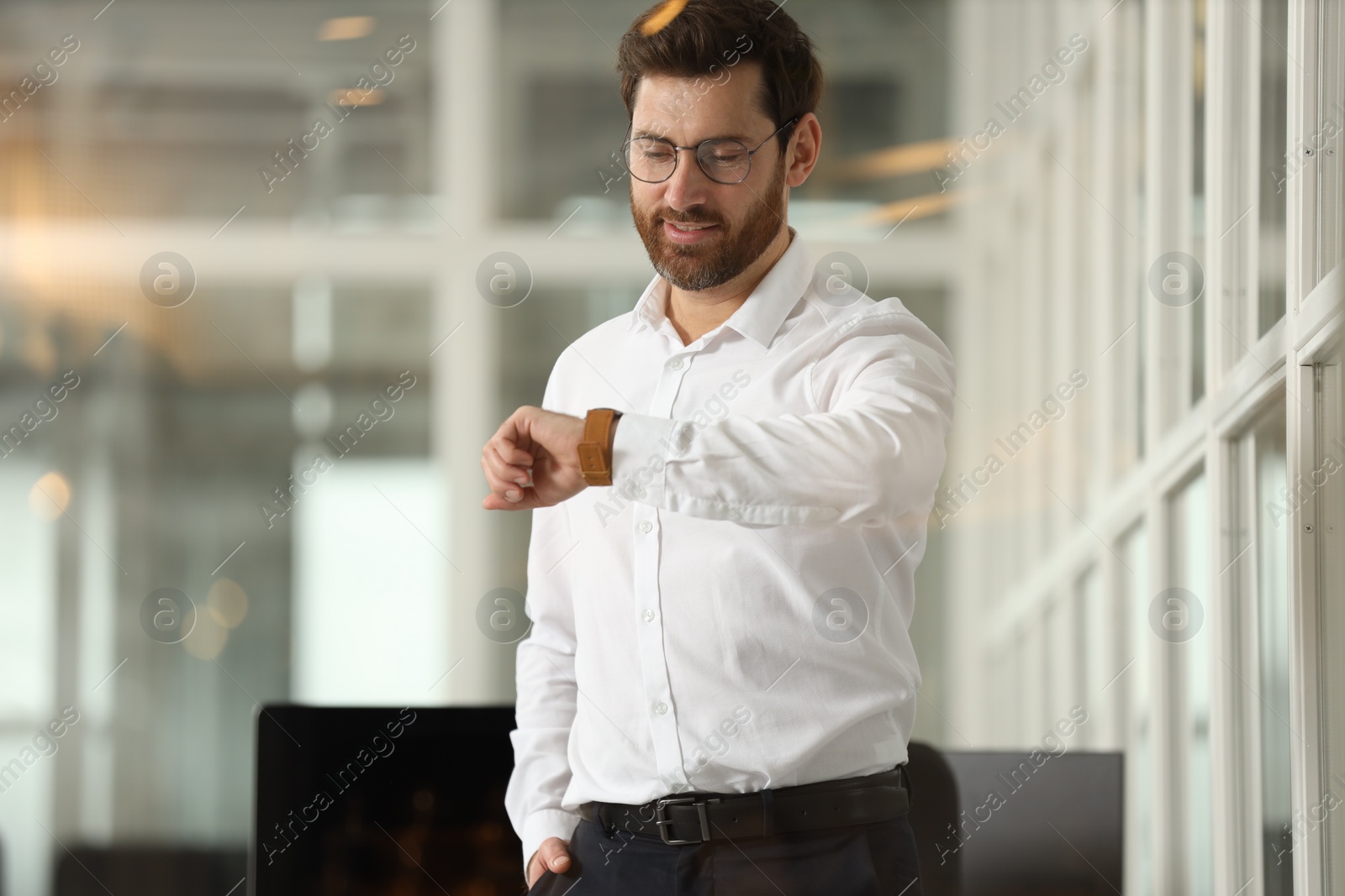 Photo of Portrait of smiling man looking at wristwatch in office. Lawyer, businessman, accountant or manager