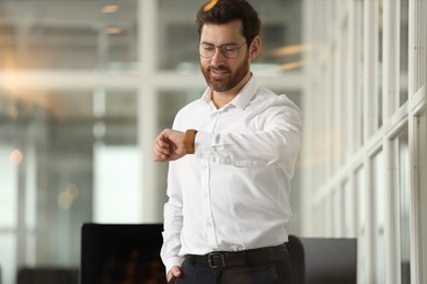 Portrait of smiling man looking at wristwatch in office. Lawyer, businessman, accountant or manager