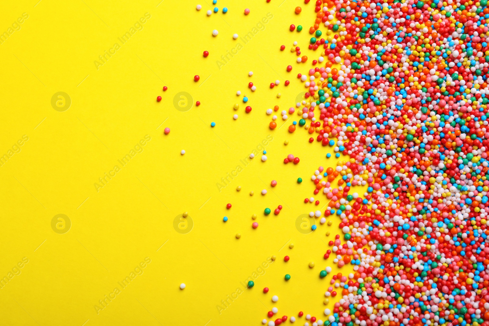 Photo of Bright colorful sprinkles on yellow background, flat lay with space for text. Confectionery decor