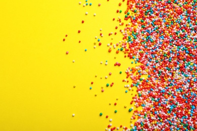 Photo of Bright colorful sprinkles on yellow background, flat lay with space for text. Confectionery decor