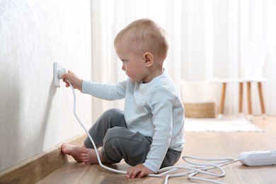 Photo of Little child playing with electrical socket and power strip plug at home. Dangerous situation