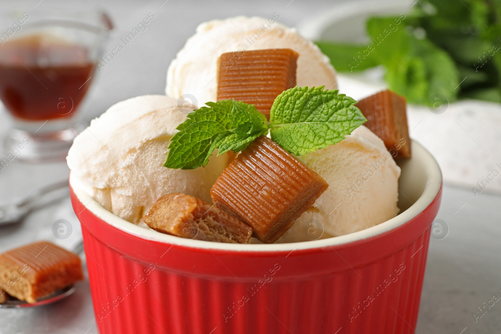 Photo of Bowl of delicious ice cream with caramel candies and mint on table, closeup