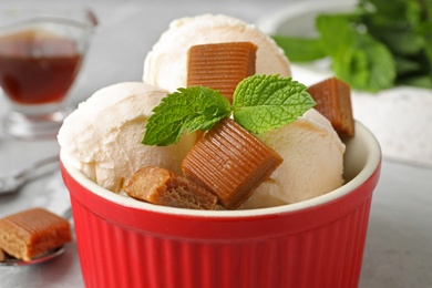 Photo of Bowl of delicious ice cream with caramel candies and mint on table, closeup