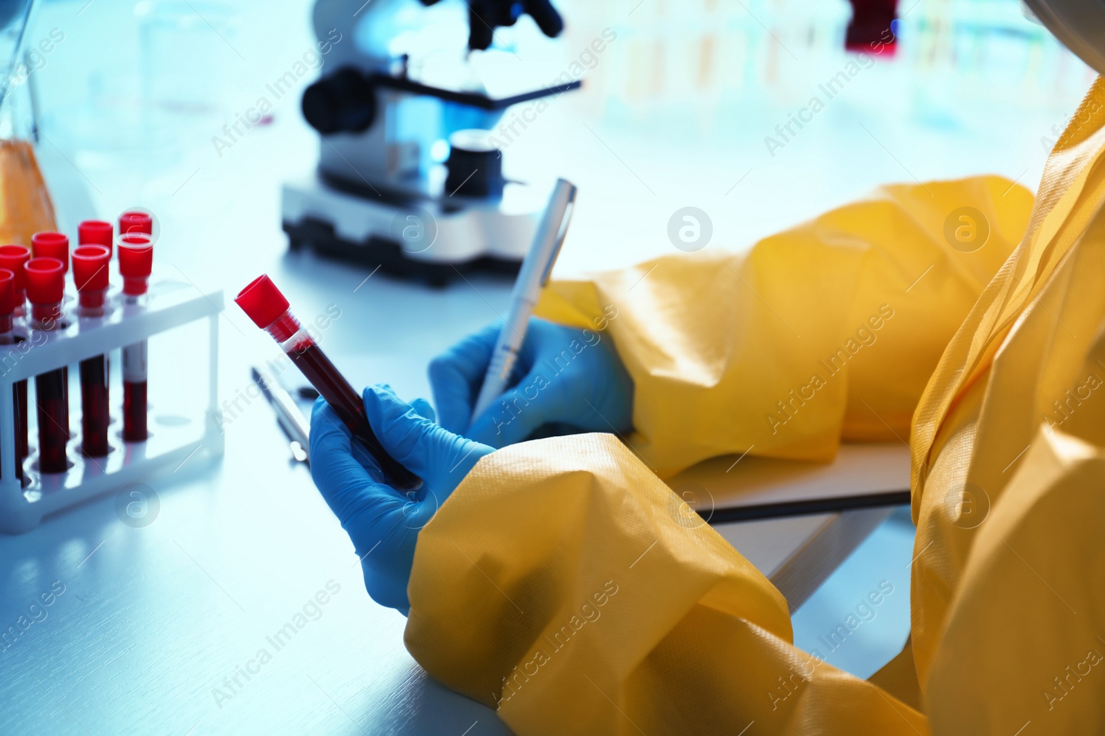 Photo of Scientist in chemical protective suit working with blood samples at table, closeup. Virus research