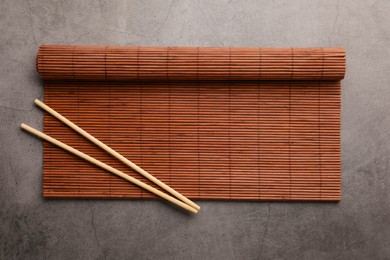 Rolled bamboo mat and chopsticks on grey table, top view. Space for text