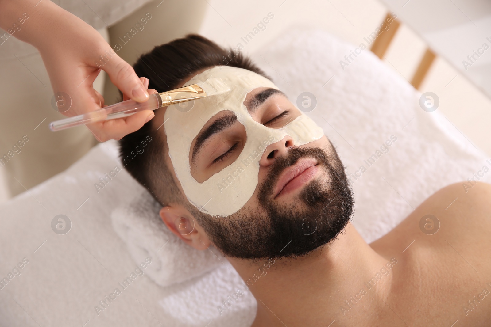 Photo of Cosmetologist applying mask on man's face in spa salon