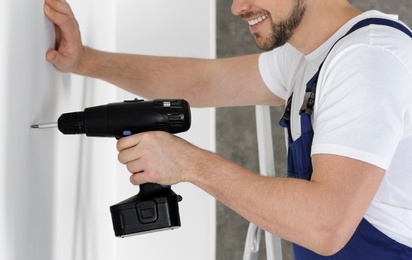 Photo of Working man using electric screwdriver indoors, closeup. Home repair