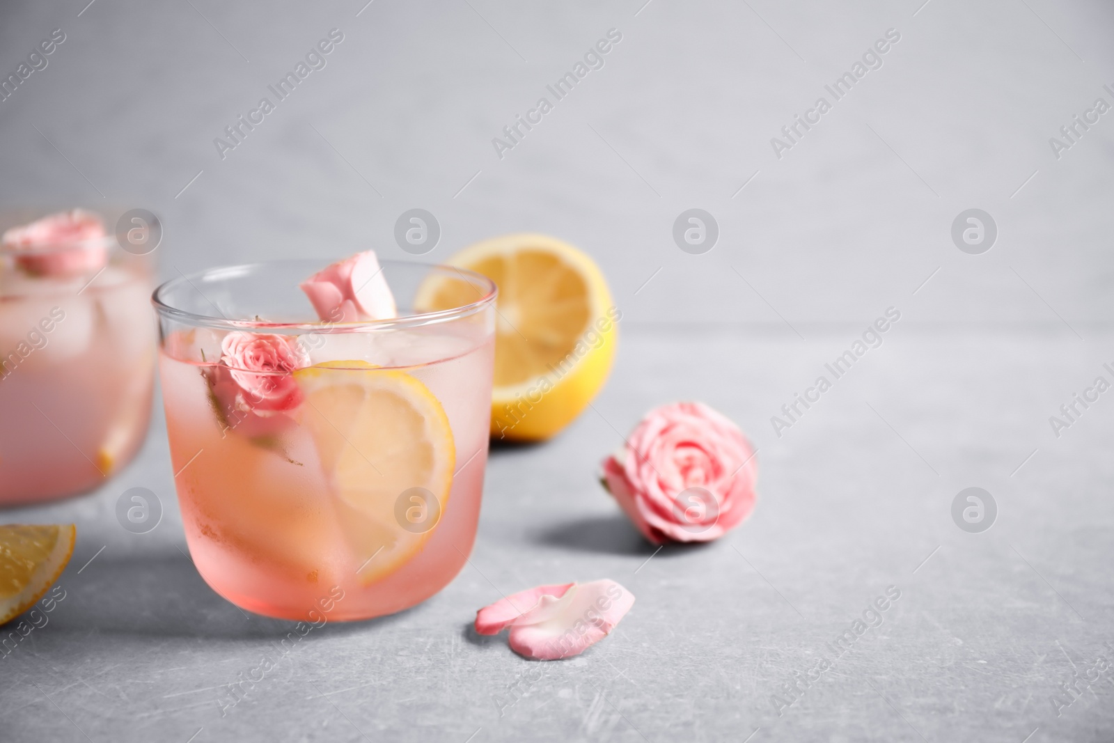 Photo of Tasty refreshing lemon drink with roses on light grey table. Space for text