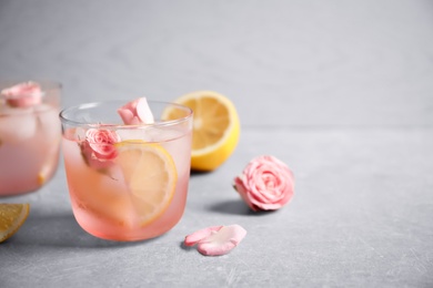 Photo of Tasty refreshing lemon drink with roses on light grey table. Space for text