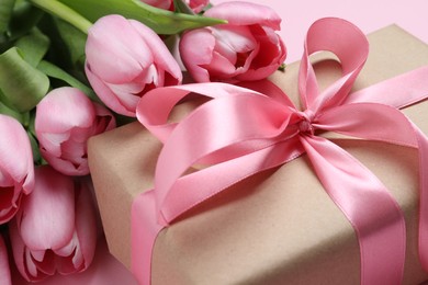 Beautiful gift box with bow and tulip flowers on pink background, closeup