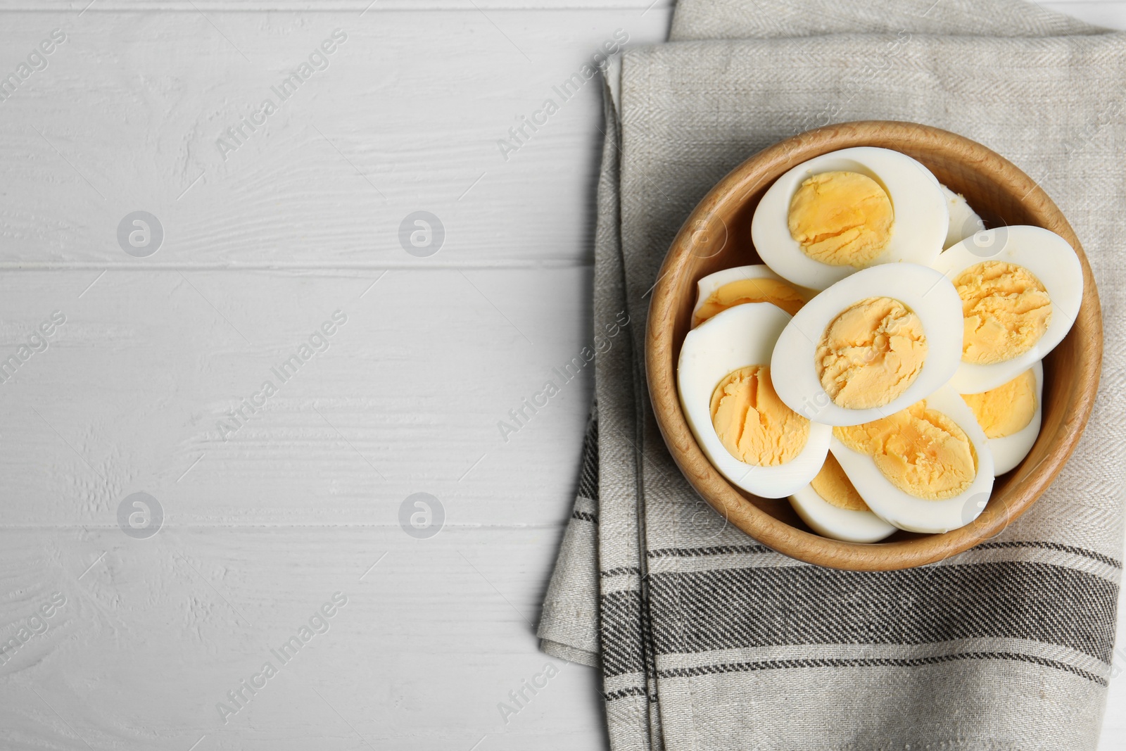 Photo of Cut hard boiled chicken eggs in bowl on white wooden table, flat lay. Space for text