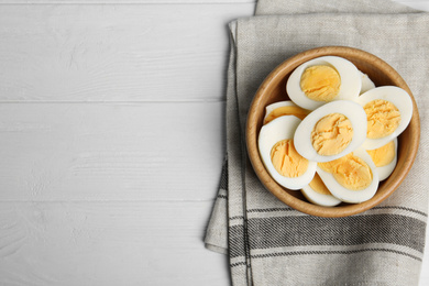 Photo of Cut hard boiled chicken eggs in bowl on white wooden table, flat lay. Space for text