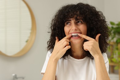Photo of Young woman applying whitening strip on her teeth in bathroom, space for text