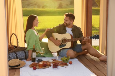 Photo of Romantic date. Beautiful woman listening to her boyfriend playing guitar during picnic outdoors