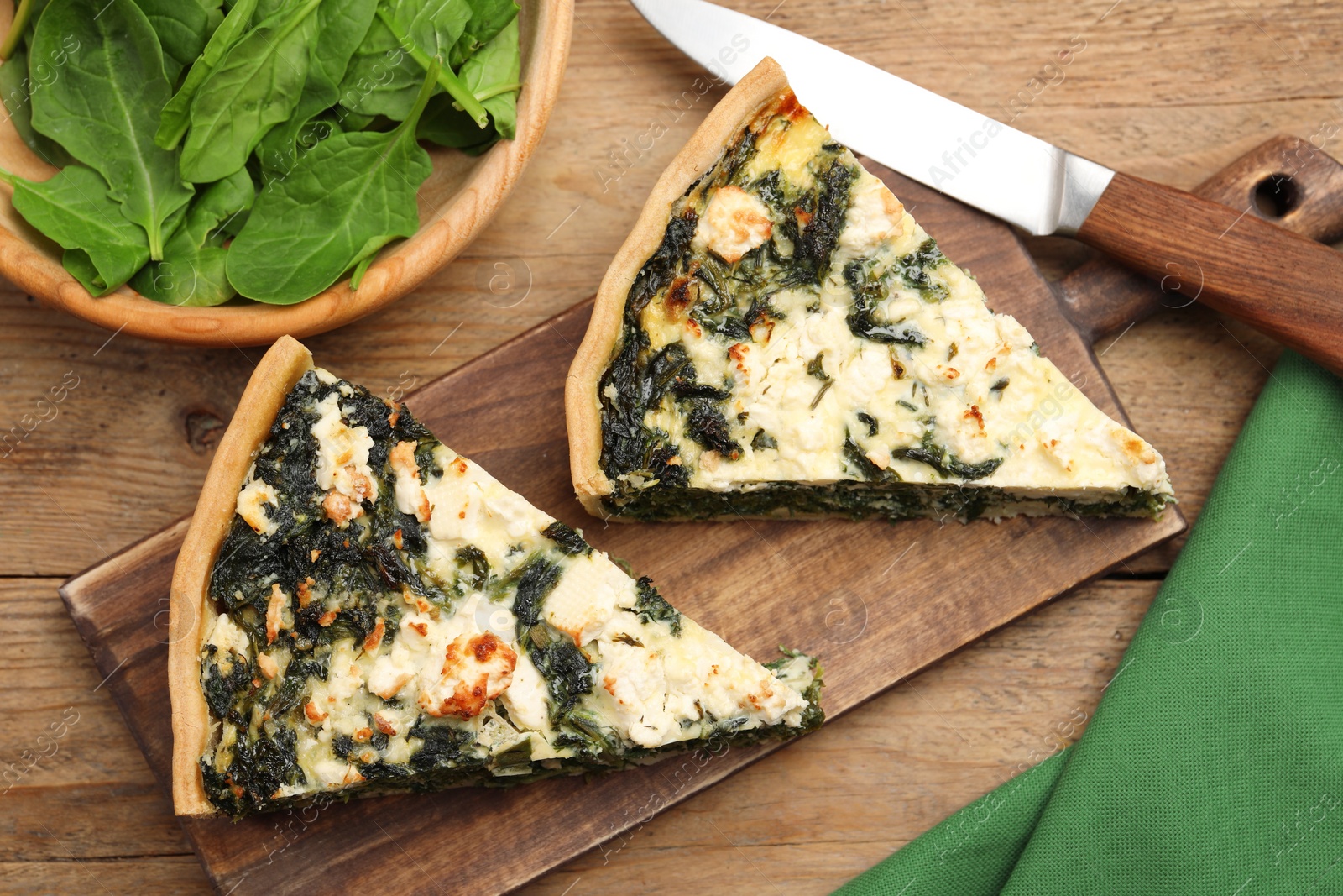 Photo of Pieces of delicious homemade quiche and fresh spinach leaves on wooden table, flat lay
