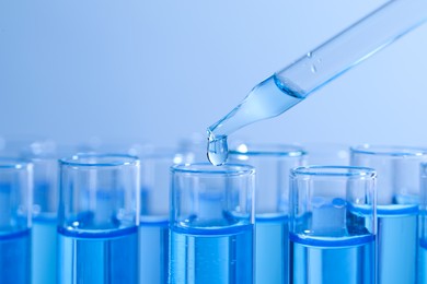 Photo of Dripping reagent into test tube on light blue background, closeup. Laboratory analysis