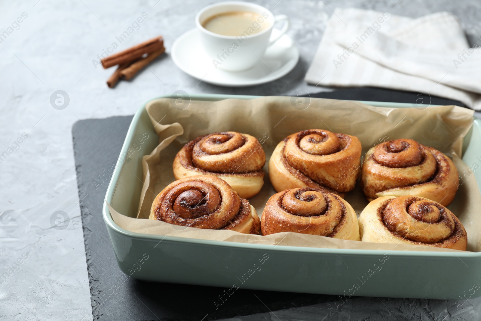 Photo of Baking dish with tasty cinnamon rolls on grey textured table, closeup