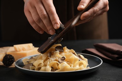 Photo of Woman slicing truffle onto tagliatelle at black table, closeup