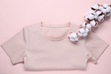 Cotton branch with fluffy flowers and t-shirt on beige background, top view