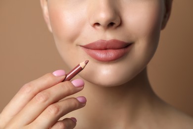 Photo of Young woman with beautiful nude lip pencil on beige background, closeup