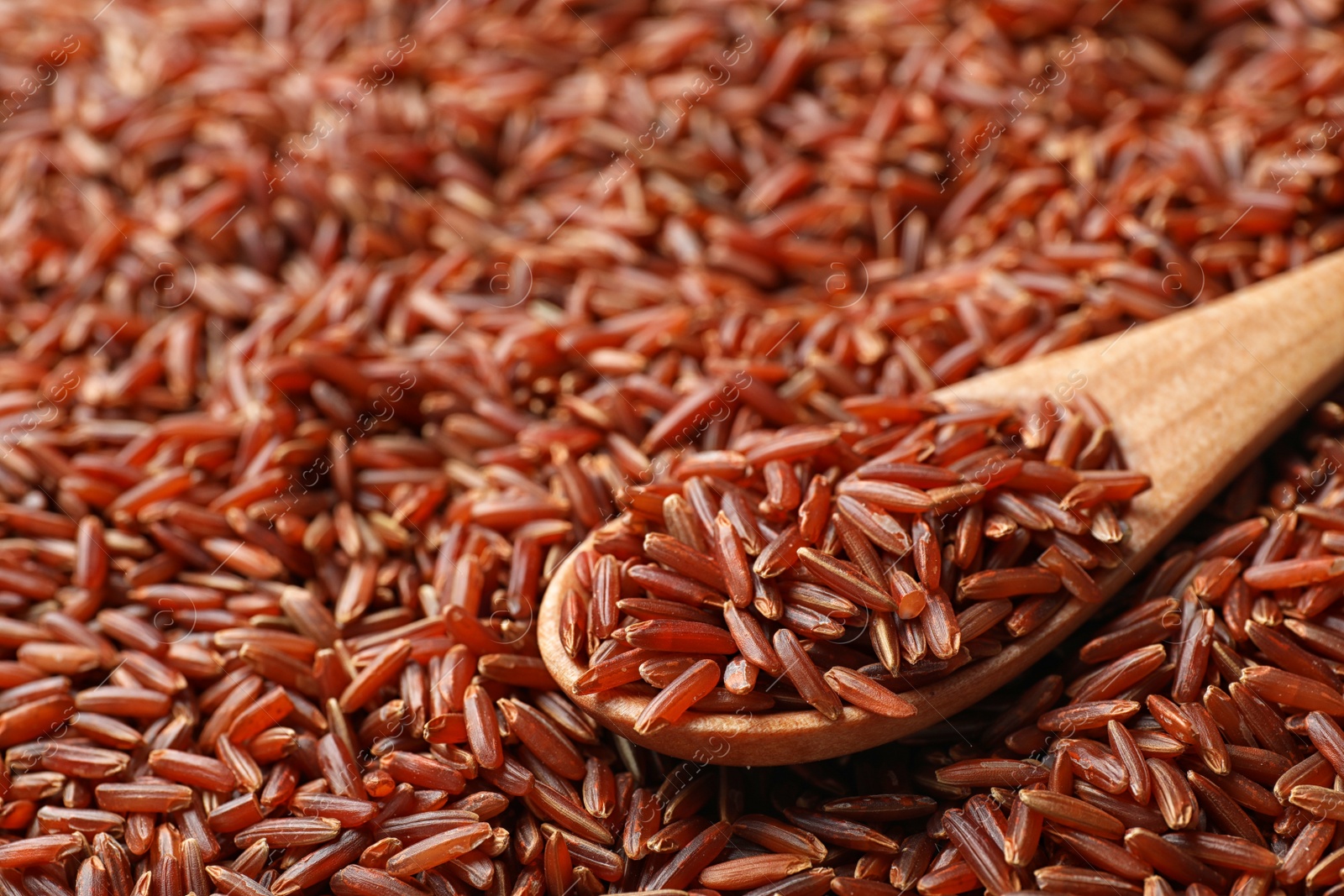 Photo of Wooden spoon with raw brown rice on cereal, closeup view