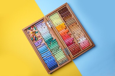 Photo of Drawing pastel set in wooden box on color background, top view