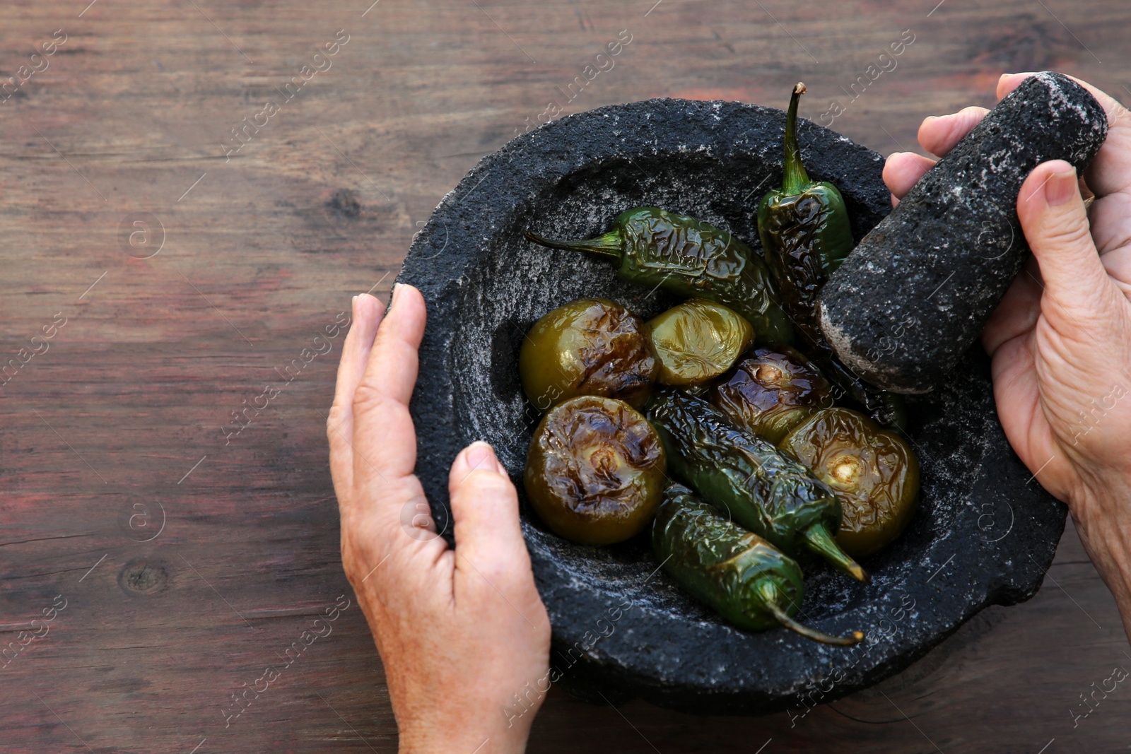 Photo of Woman grinding vegetables in mortar at wooden table, above view. Ingredients for salsa sauce