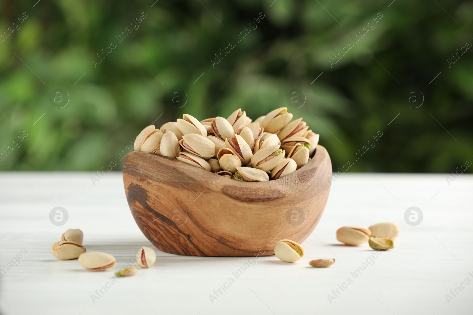 Photo of Tasty pistachios in bowl on white table against blurred background